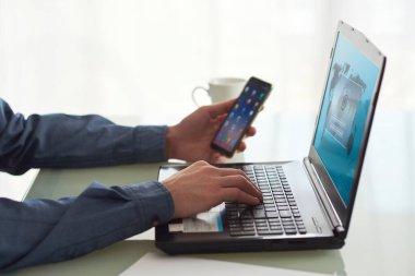 Bilgisayarı ve akıllı telefonuyla çalışan bir işçinin kapalı planı. Çalışma ortamını, teknolojiyi temsil ediyor..