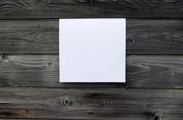 Blank sheet of paper on vintage wooden background. White paper with plenty of copy space. Blank paperwork template for design portfolios. Top view.