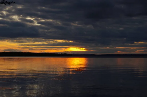 Himmelspanorama bei Sonnenuntergang. helle Sonnenlinie vor dunklem Wolkenhintergrund. Reflexion auf einem Wasser. — Stockfoto