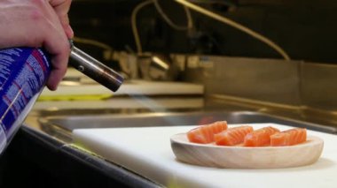 Suşi yapan bir adam mutfak meşalesiyle somon pişiriyor. Suşi rulosu hazırlıyor. Japon mutfak aletleri ile profesyonel aşçı..