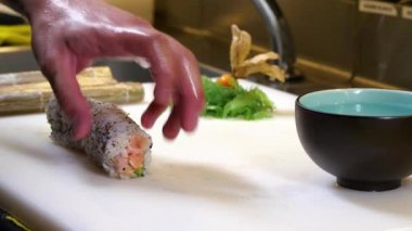 Suşi yapan biri somon balığı ve avokado suşi böreği keser. Japon mutfağı. Mutfak aletleriyle profesyonel aşçı..