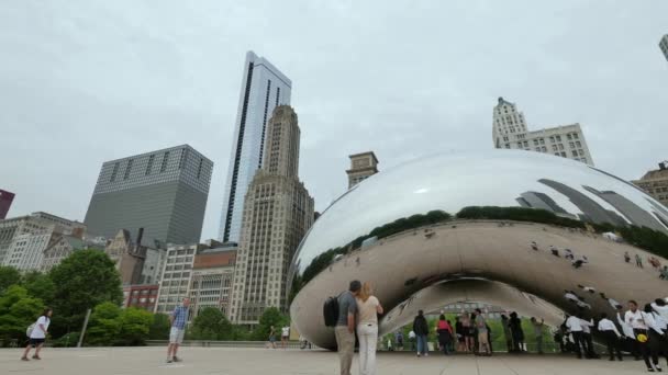 Turystów w Chicago Bean pomnik w parku Millennium. Tłumy odwiedzających Millennium Park w Chicago. Panoramy Chicago wznosi się w tle. Film pokazujący punkt orientacyjny w Illinois, przesuwanie w prawo. — Wideo stockowe