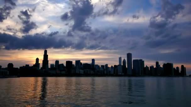 シカゴのスカイラインはシカゴ ダウンタウンの高層ビルは夜に夕焼け雲の動きからミシガン湖に映る夕日の時間経過のビデオ時間経過で湖面に映る アメリカ合衆国の私たちの夜シカゴ シティ センター スカイライン畏敬の念します — ストック動画