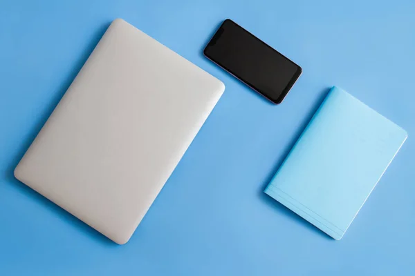 Laptop on a blue background. Laptop and bottle on a blue background. Laptop phone and notepad on a blue background. Laptop phone, notepad and bottle on a blue background.