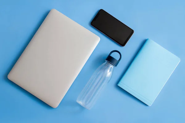 Laptop on a blue background. Laptop and bottle on a blue background. Laptop phone and notepad on a blue background. Laptop phone, notepad and bottle on a blue background.