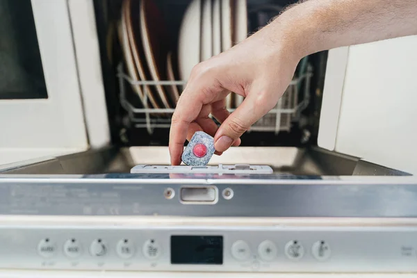 Open dishwasher with clean utensils in white kitchen.