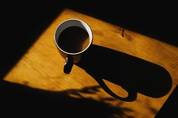 Kubek kawy, z którego wychodzi duży cień na drewnianym stole — Zdjęcie stockowe