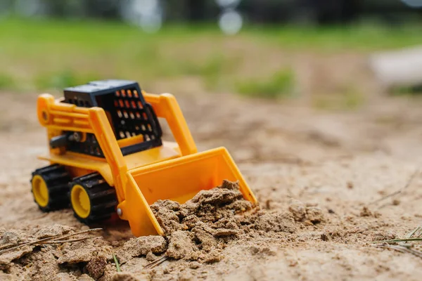 A játékrakodó homokot ás. A gyerek a homokozóban hagyta a játékot. — Stock Fotó
