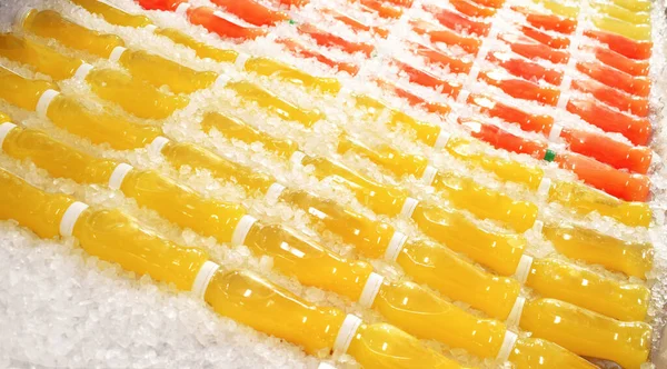 Yellow and red juice bottles in ice. Fruit juice in freezer.