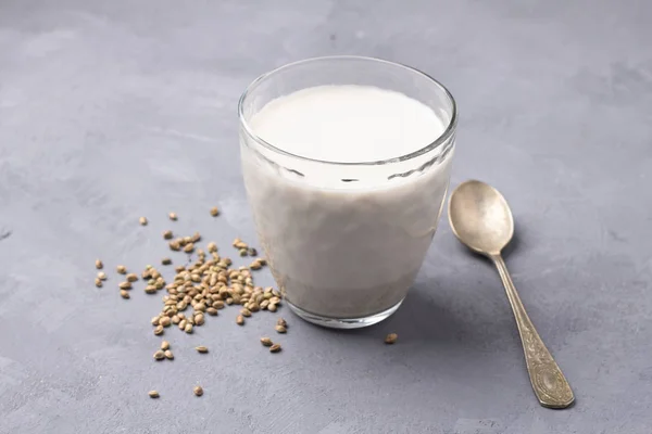 Hemp seeds in a wooden bowl and hemp milk on gray background