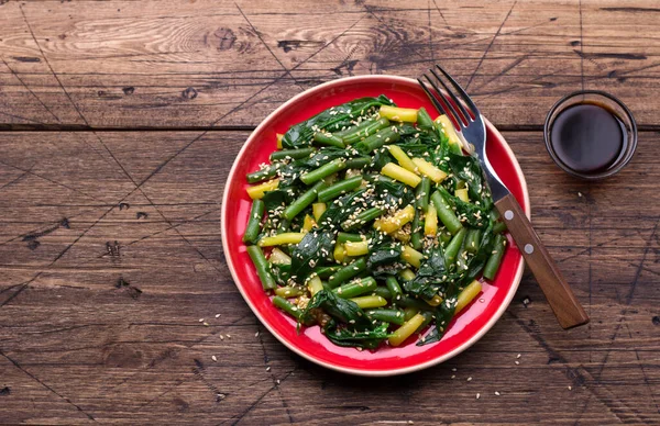 Green and yellow beans with spinach, sesame seeds and soy sauce on wooden table