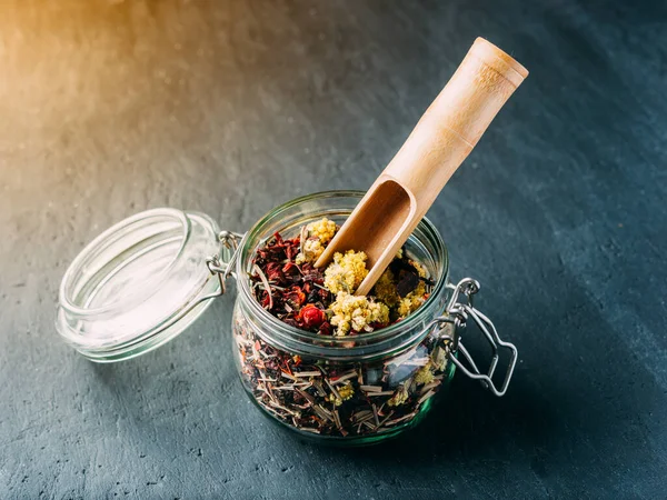 Herbal and fruit teas in glass jars on a dark background. Medicinal herbs. A natural, eco product.Wooden spatula tea spoon.