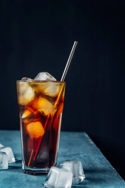 Cold brew coffee in a glass with metal straw on a dark background.Iced coffee with ice cube.