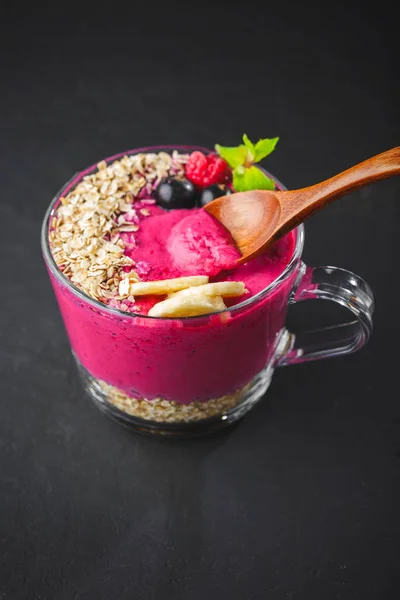 Healthy breakfast,fitness food for diet, Raspberry and currant berry bowl smoothie in a one glass cup with a wooden spoon,mint leaf, oatmeal in white dish on a dark background.