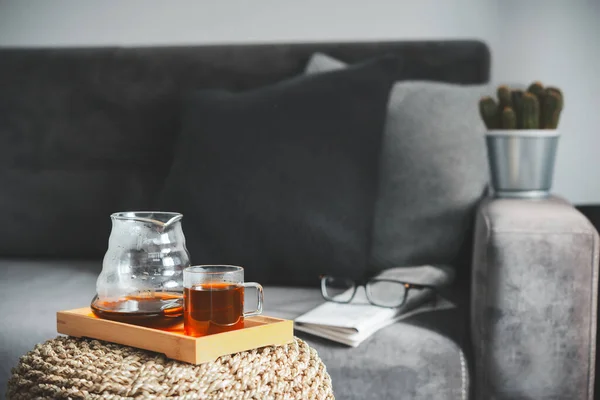 Fresh coffee brewed by an alternative method in a glass teapot on a wooden tray against a gray sofa