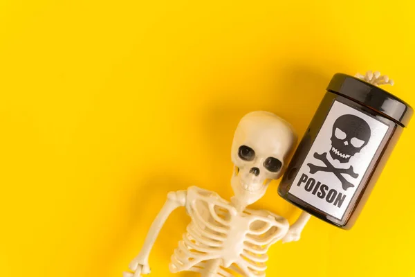 Concept of poison, toxic substances, drug overdose, lethal dose,glass jar with skull and crossbonesl and skeleton on yellow background,copy space