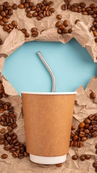 Recycled paper Cup with metal straw on blue paper background and Scattered Arabica coffee beans on brown recycled Kraft paper for packaging