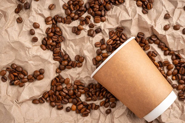 Recycled paper Cup and Scattered Arabica coffee beans on brown recycled Kraft paper for packaging