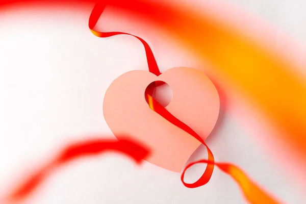 Heart cut out of paper, with a tied ribbon in focus in the foreground, white background, symbol of Valentine\'s Day
