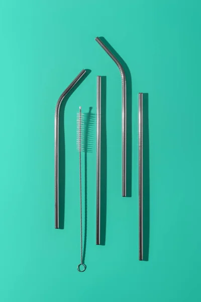 Metal reusable cocktail tubes, minimalistic zero waste concept and eco friendly, emerald background
