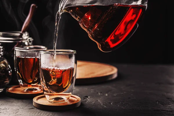 Process brewing tea,tea ceremony,Cup of freshly brewed black tea, dark moody.Hot water is poured from the kettle into a flass cup on a black concrete background,copy space.