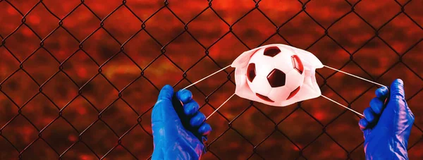 Concept banner Cancellation of the football championship due to a coronavirus quarantine.Medical mask with soccers ball in the hands of a medic in blue gloves. Novel coronavirus,2019nCoV, outbreak