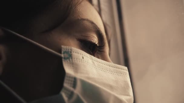 Sjuk flicka i mask tittar ut genom fönstret under karantänen.Närbild. — Stockvideo