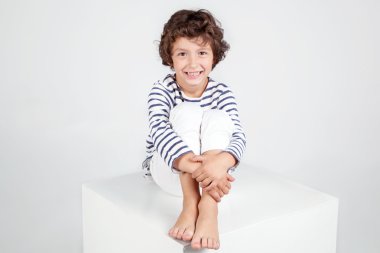 Küp üzerinde oturan ve kameraya bakarak sevimli kıvırcık gülümseyen çocuk.