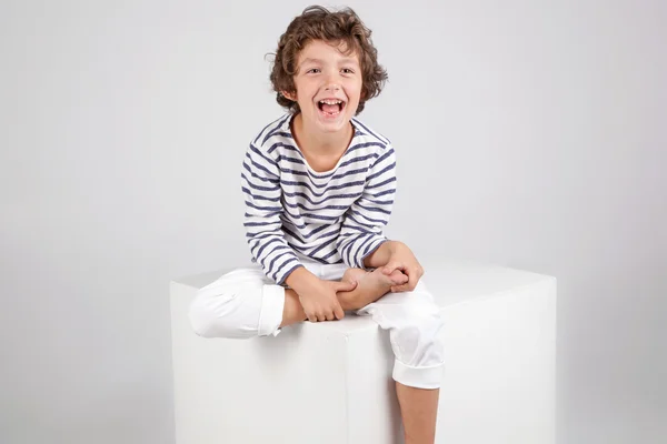 Happy laughing curly boy sitting over white background. Fashion — Stock Photo, Image