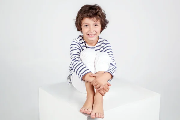 Lindo niño rizado sonriente sentado en el cubo y mirando a la cámara . —  Fotos de Stock