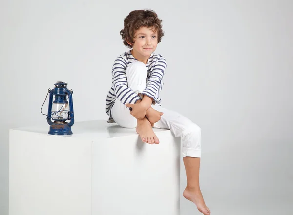 Malý módní chlapec sedí nad bílým pozadím. — Stock fotografie