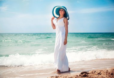 Uzun beyaz elbiseli sahilde yürüyen güzel genç kadın bir