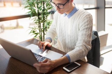 Gözlüklü genç adam onun laptop ve cep kafede kullanın. Serbest meslek