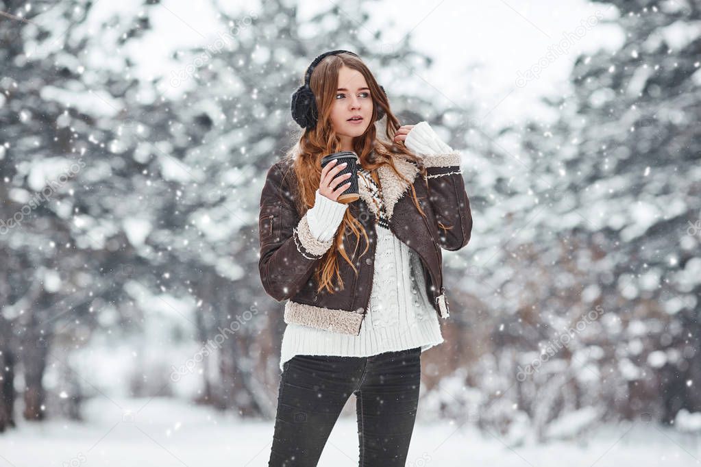 Happy young woman with cup of coffee in snowy winter day. Girl e