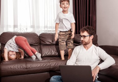 Genç baba çocuklarıyla evde çalışmaya çalışıyor. Kendini soyutlama. Evde kal konsepti. Serbest Çalışan.