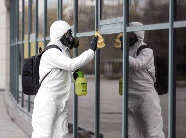 Karantina, koronavirüs enfeksiyonu. Koruyucu ekipman kullanan bir adam şehirde dezenfektanla dezenfekte ediyor. Sokakta temizlik ve dezenfeksiyon. Koruyucu giysi ve maske. Salgın.