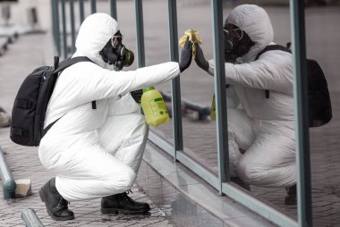 Karantina, koronavirüs enfeksiyonu. Koruyucu ekipman kullanan bir adam şehirde dezenfektanla dezenfekte ediyor. Sokakta temizlik ve dezenfeksiyon. Koruyucu giysi ve maske. Salgın.