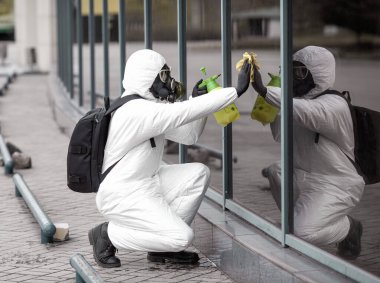 Karantina, koronavirüs enfeksiyonu. Koruyucu ekipman kullanan bir adam şehirde dezenfektanla dezenfekte ediyor. Sokakta temizlik ve dezenfeksiyon. Koruyucu giysi ve maske. Salgın.