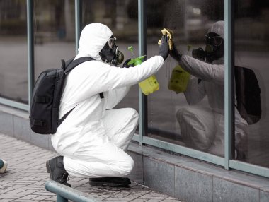 Karantina, koronavirüs enfeksiyonu. Koruyucu ekipman kullanan bir adam şehirde dezenfektanla dezenfekte ediyor. Sokakta temizlik ve dezenfeksiyon. Koruyucu giysi ve maske. Salgın.