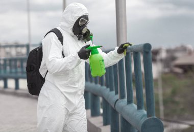 Karantina, koronavirüs enfeksiyonu. Koruyucu ekipman kullanan bir adam şehirde dezenfektanla dezenfekte ediyor. Sokakta temizlik ve dezenfeksiyon. Koruyucu giysi ve maske. Salgın.