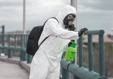 Karantina, koronavirüs enfeksiyonu. Koruyucu ekipman kullanan bir adam şehirde dezenfektanla dezenfekte ediyor. Sokakta temizlik ve dezenfeksiyon. Koruyucu giysi ve maske. Salgın.