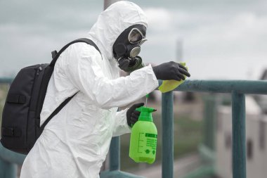 Karantina, koronavirüs enfeksiyonu. Koruyucu ekipman kullanan bir adam şehirde dezenfektanla dezenfekte ediyor. Sokakta temizlik ve dezenfeksiyon. Koruyucu giysi ve maske. Salgın.