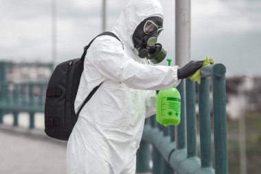 Karantina, koronavirüs enfeksiyonu. Koruyucu ekipman kullanan bir adam şehirde dezenfektanla dezenfekte ediyor. Sokakta temizlik ve dezenfeksiyon. Koruyucu giysi ve maske. Salgın.