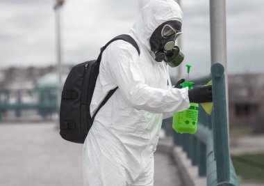 Karantina, koronavirüs enfeksiyonu. Koruyucu ekipman kullanan bir adam şehirde dezenfektanla dezenfekte ediyor. Sokakta temizlik ve dezenfeksiyon. Koruyucu giysi ve maske. Salgın.