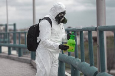 Karantina, koronavirüs enfeksiyonu. Koruyucu ekipman kullanan bir adam şehirde dezenfektanla dezenfekte ediyor. Sokakta temizlik ve dezenfeksiyon. Koruyucu giysi ve maske. Salgın.