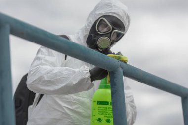 Karantina, koronavirüs enfeksiyonu. Koruyucu ekipman kullanan bir adam şehirde dezenfektanla dezenfekte ediyor. Sokakta temizlik ve dezenfeksiyon. Koruyucu giysi ve maske. Salgın.