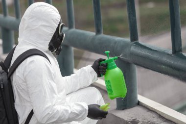 Karantina, koronavirüs enfeksiyonu. Koruyucu ekipman kullanan bir adam şehirde dezenfektanla dezenfekte ediyor. Sokakta temizlik ve dezenfeksiyon. Koruyucu giysi ve maske. Salgın.