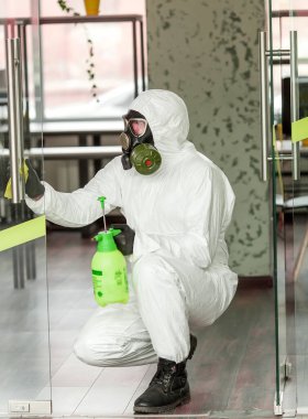 Koruyucu ekipmanlı bir adam ofiste spreyle dezenfekte ediyor. Coronavirus covid-19 hastalığından dolayı yüzey tedavisi. Beyaz takım elbiseli bir adam odayı sprey silahla dezenfekte ediyor. Virüs salgını