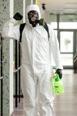 Koruyucu ekipmanlı bir adam ofiste spreyle dezenfekte ediyor. Coronavirus covid-19 hastalığından dolayı yüzey tedavisi. Beyaz takım elbiseli bir adam odayı sprey silahla dezenfekte ediyor. Virüs salgını