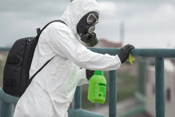 Quarantine, coronavirus infection. A man in protective equipment disinfects with a sprayer in the city. Cleaning and Disinfection at the street. Protective suit and mask. Epidemic.